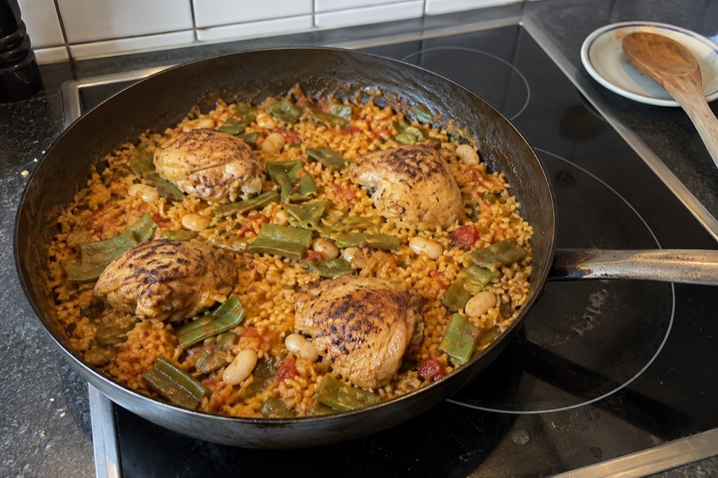 Paella con pollo e fagiolini su un piano cottura in vetroceramica domestico